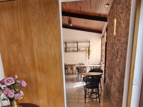 Sala de refeições com mesas e cadeiras, vista da porta de madeira