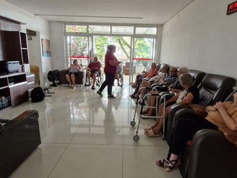 Sala de estar com poltronas reclináveis, com residentes e profissional em atividade