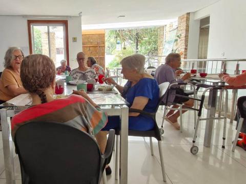 Residentes em refeição à mesa, em ambiente iluminado